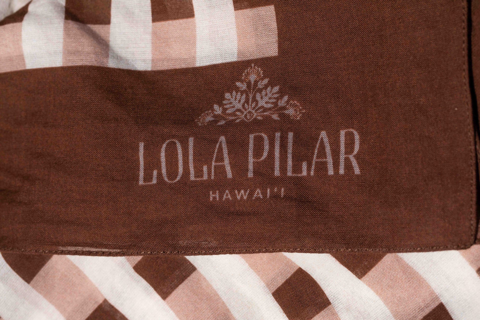 Brown fabric with 'Lola Pilar Hawaii' logo on a checkered background