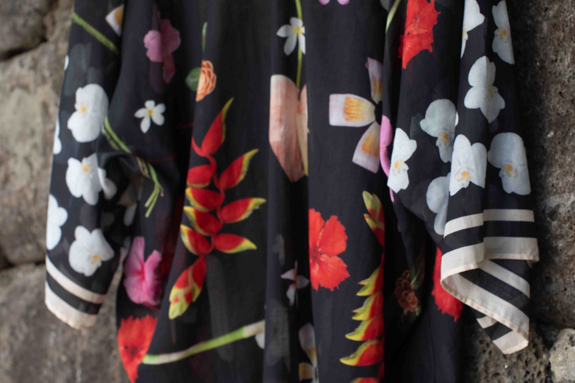 Lola Pilar black cotton kimono top with flowing Hawaiian floral print featuring hibiscus, torch ginger, heliconia, plumeria, and banana flowers, designed in Hawaii and made in Italy for effortless resort layering.