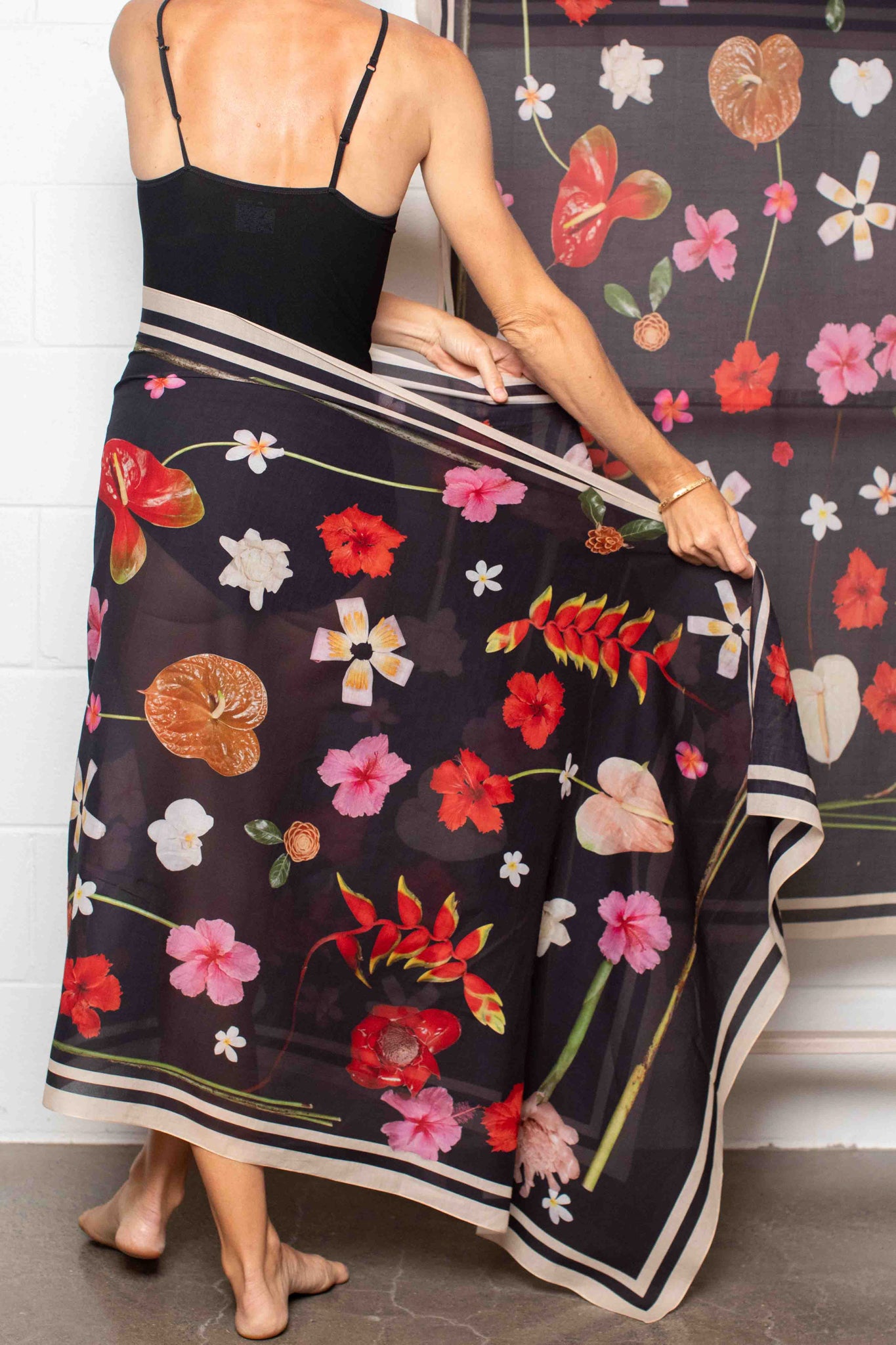 Hawaiian floral wrap with black background showcasing hibiscus blooms, hanging heliconia, banana flowers, and plumeria in vibrant tropical shades