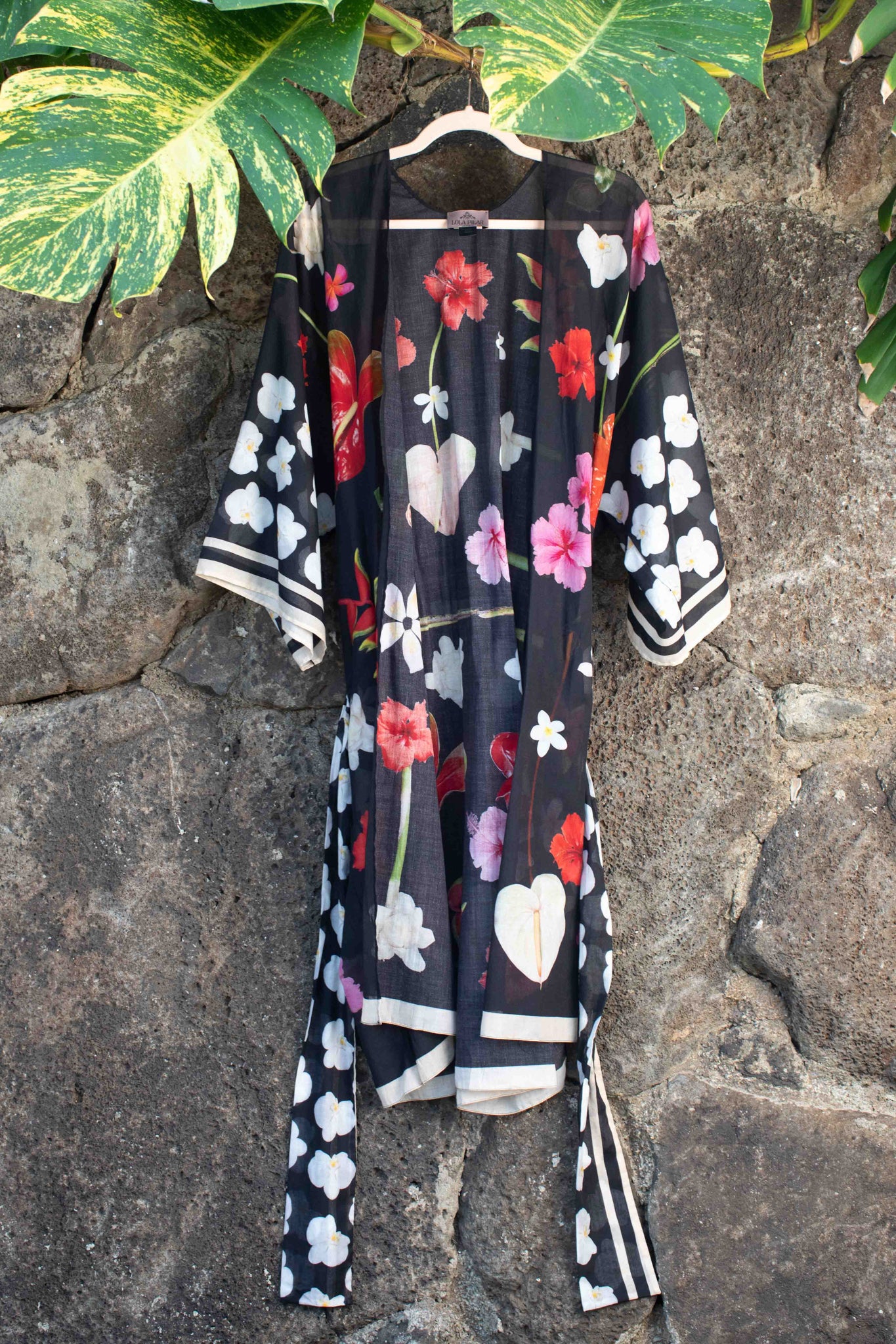 Lola Pilar black cotton kimono robe with vibrant Hawaiian floral artwork featuring hibiscus, torch ginger, heliconia, plumeria, and banana flowers, designed for elevated resort and travel style.