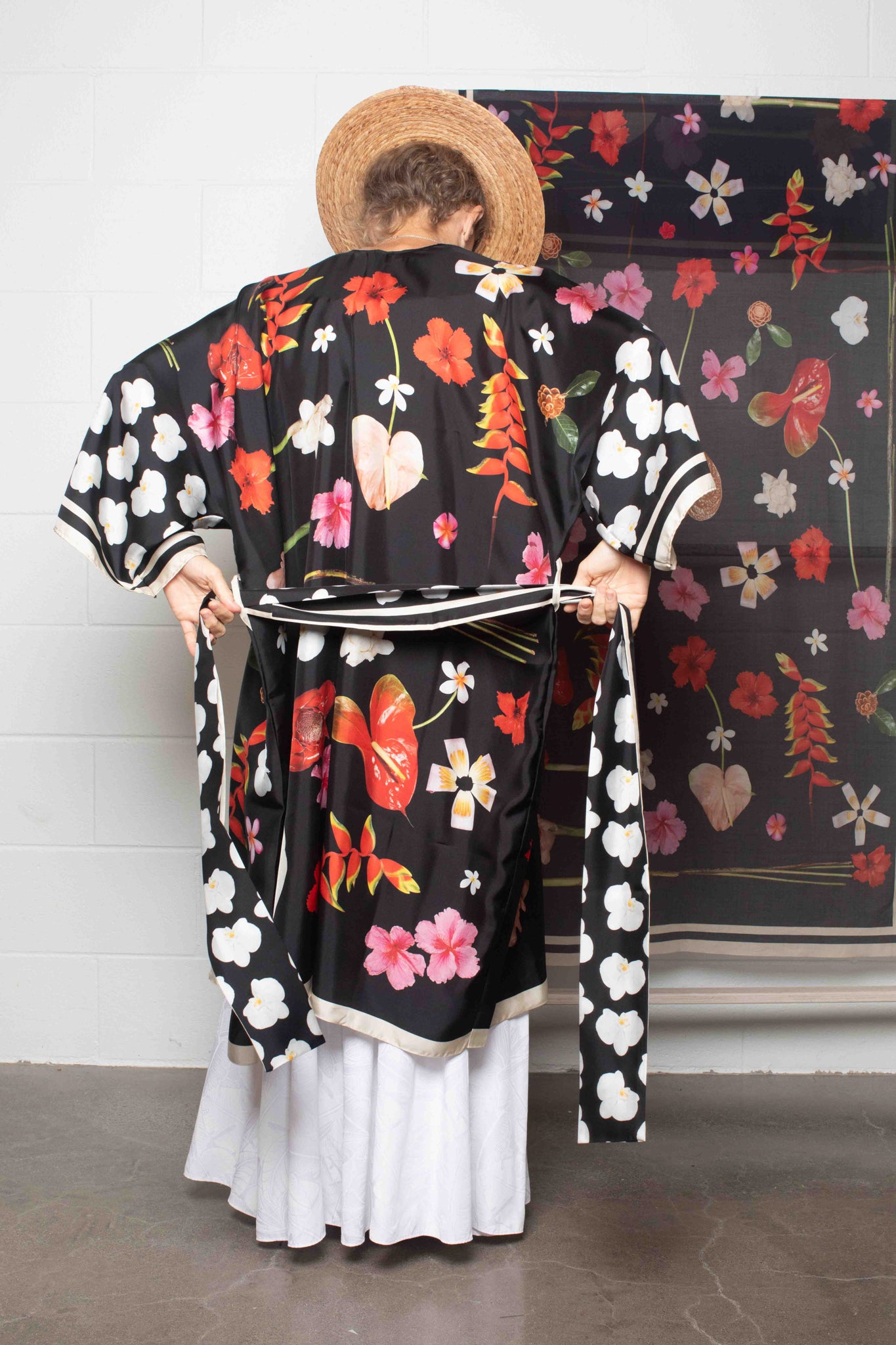 Elegant black silk kimono robe by Lola Pilar with vivid Hawaiian floral print featuring hibiscus, torch ginger, heliconia, plumeria, and banana flowers for refined resort style.