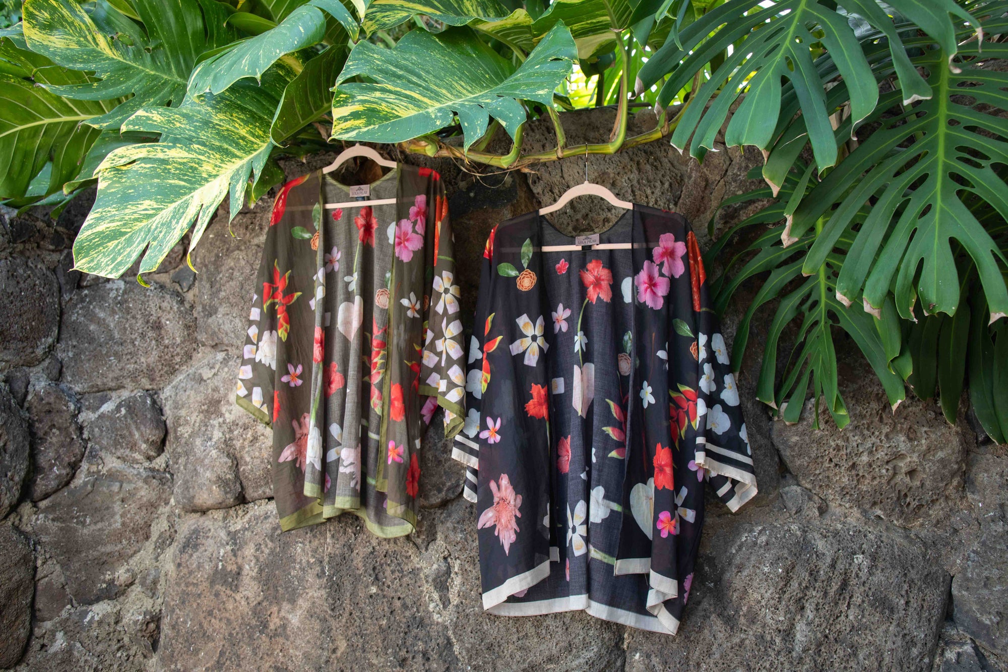 Elegant black cotton kimono top with vibrant tropical Hawaiian botanical design in pink, yellow, red, and white tones, created by Lola Pilar for refined travel and resort wear.

