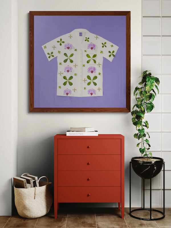photograph of an aloha shirt art print with a purple background set in a hallway with a dresser, plant, and basket in someones home.