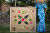 Woman in a Hawaiian mumu holding a large 4ftx4ft print called Tutu&#39;s Quilt inspired by the Hawaiian quilt