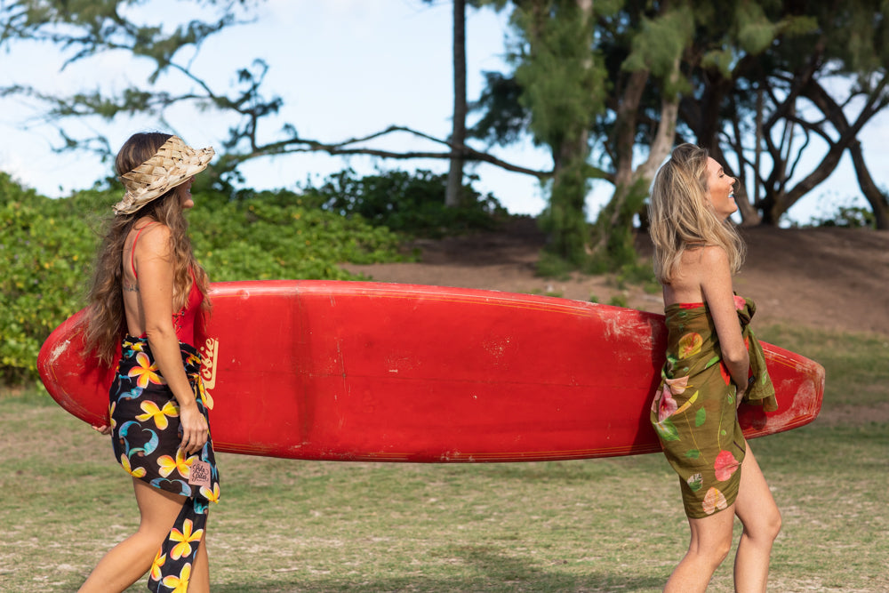 two ladies laughing heading out for a surf in their lola pilar hawaii cotton pareos, made in italy